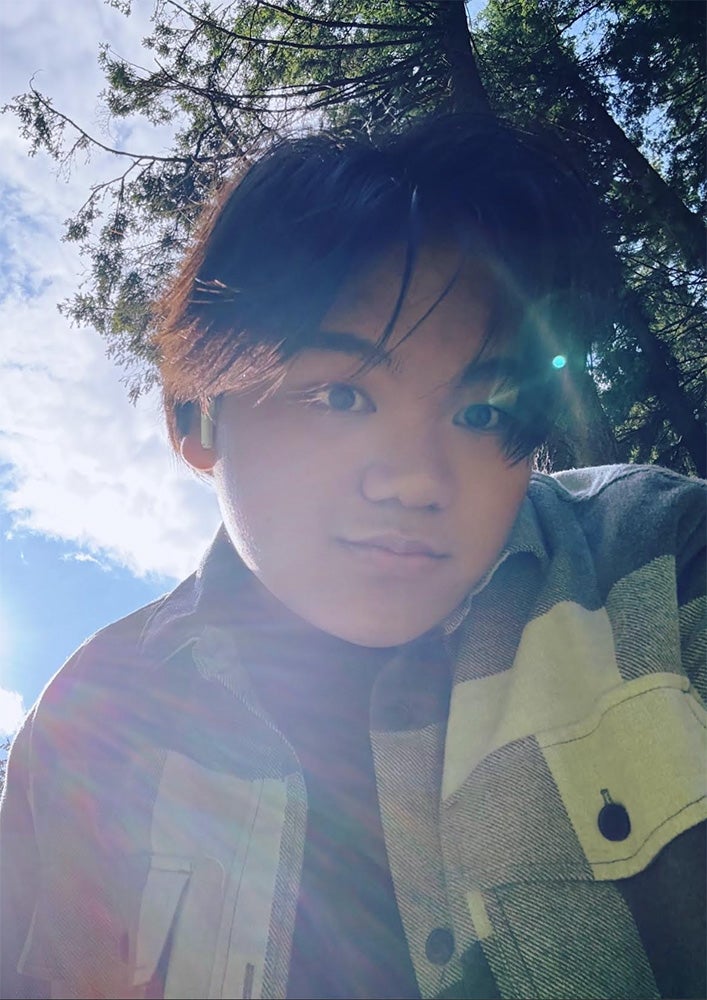 Image of young man selfie looking upward with blue sky and fir trees in the background