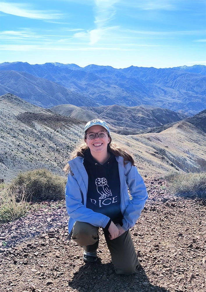 Image of young woman squatting on top of a mountain with mountains in the background