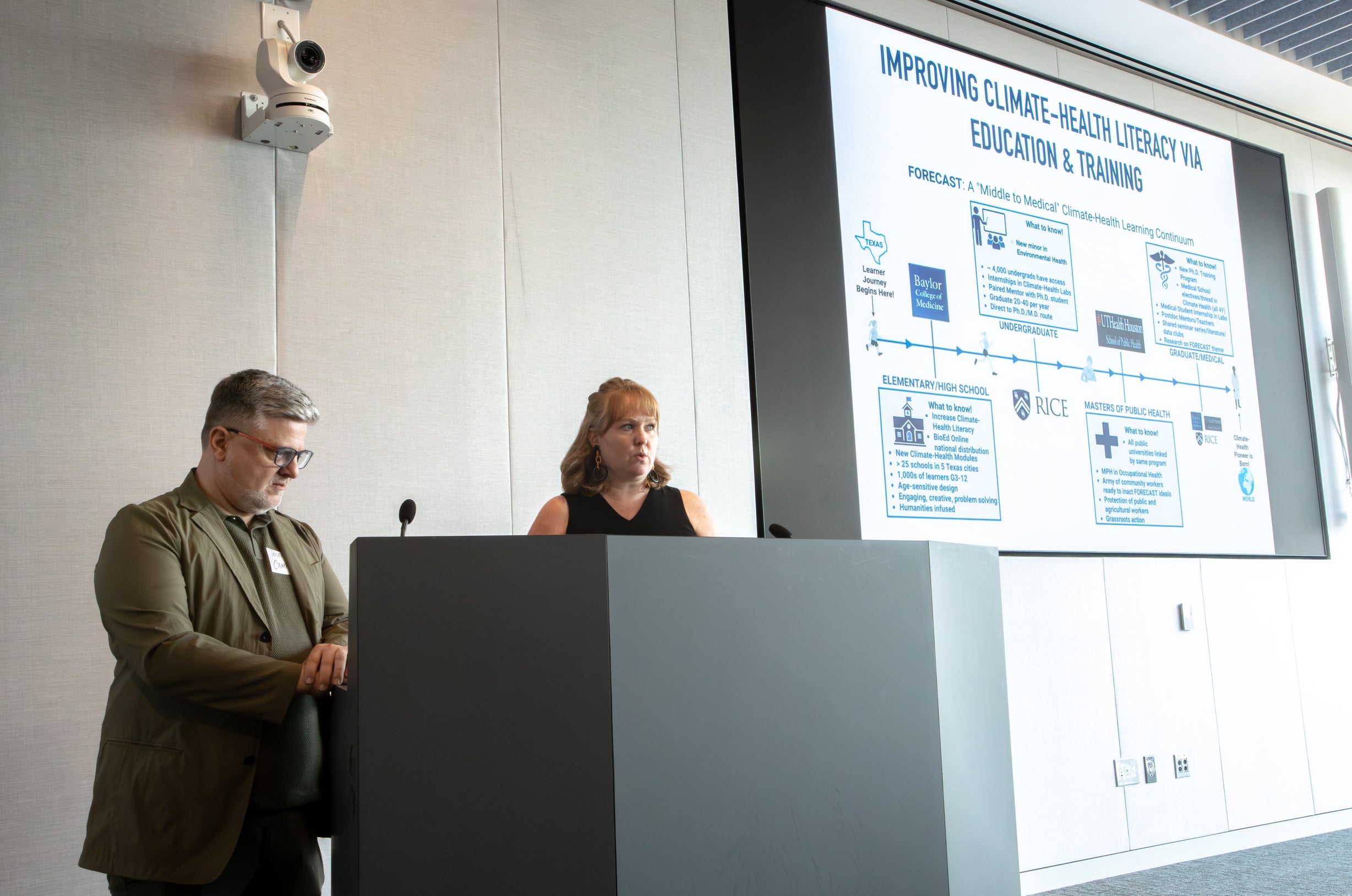 Photo of two people behind a podium with a projection screen to the right.