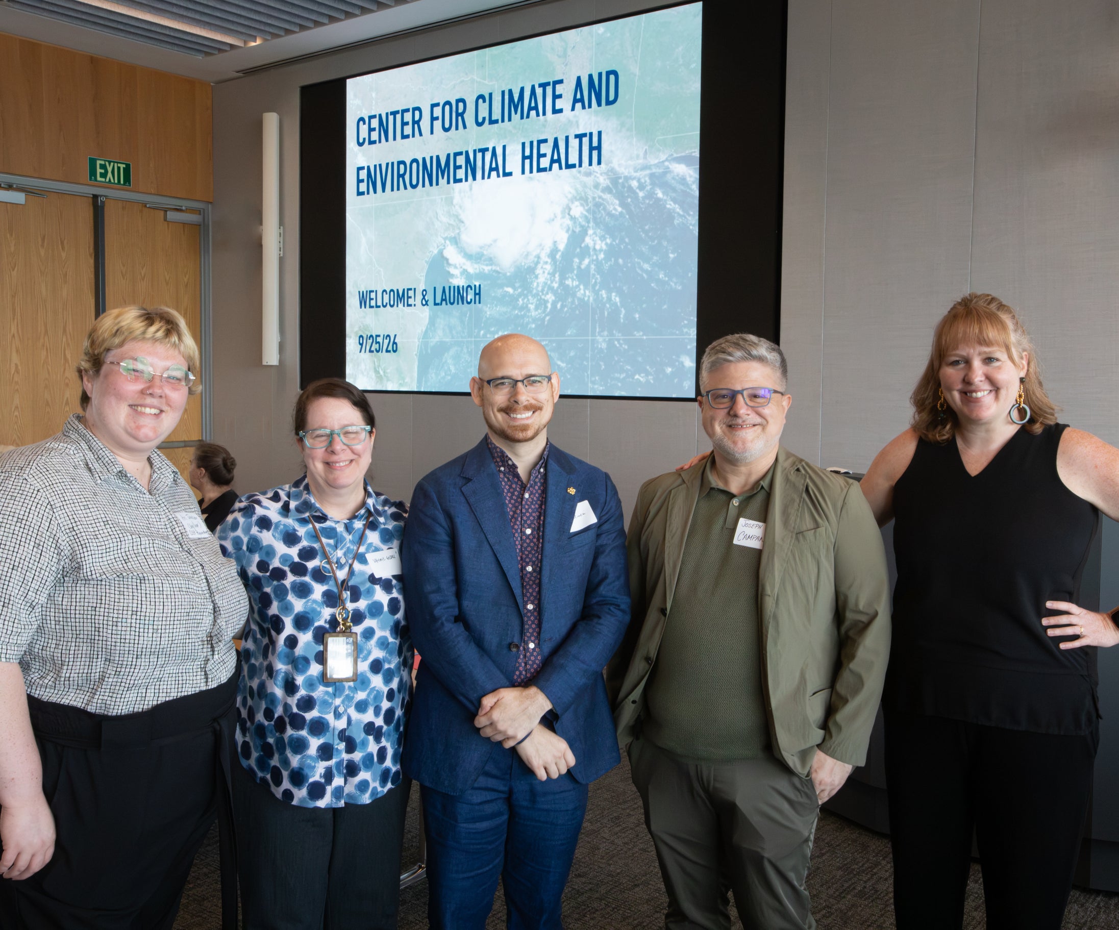 Photo of 5 CCEH organizers standing and smiling in front of projector screen